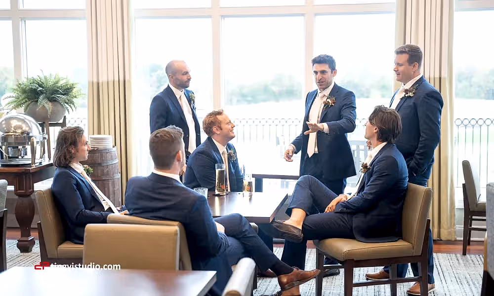 Groomsmen sitting around a table talking in navy blue suits.