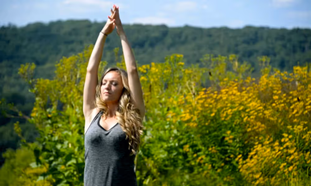 Women stretching with hands upward toward sky standing in front of yellow flowers.