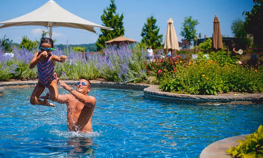 Young girl midair as her father throws her in pool.