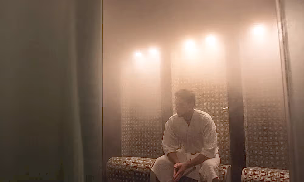 Man in white bath robe sitting in steamy sauna.