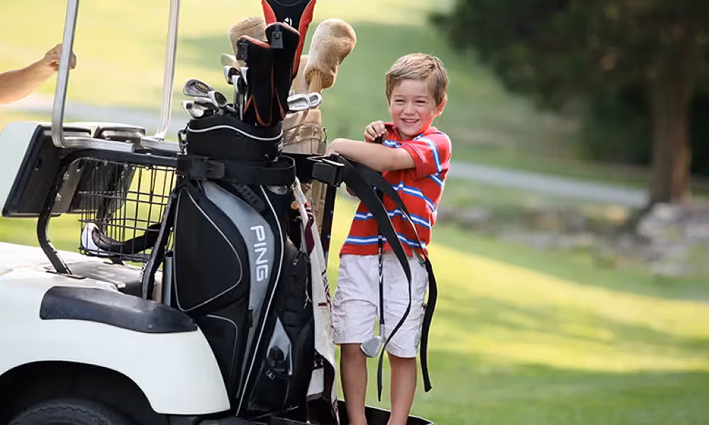 Little boy standing on the back of a golf cart