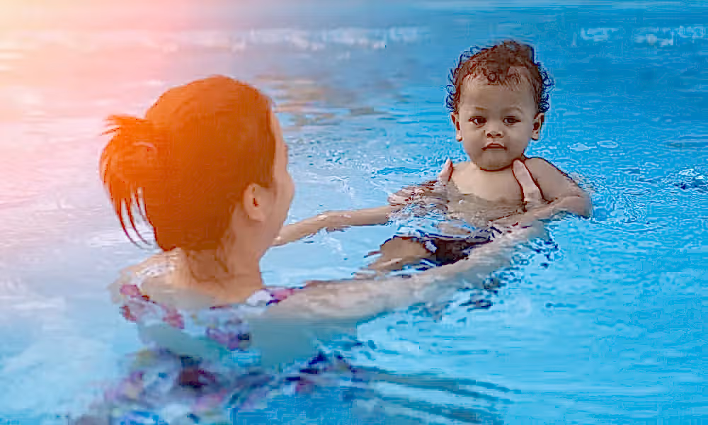 Woman holding baby in pool.