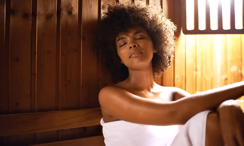 Woman in white towel sitting in sauna.