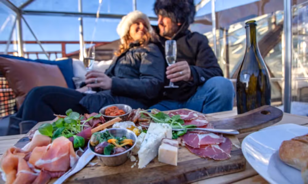 Couple sitting in champagne chalet enjoying charcuterie board.