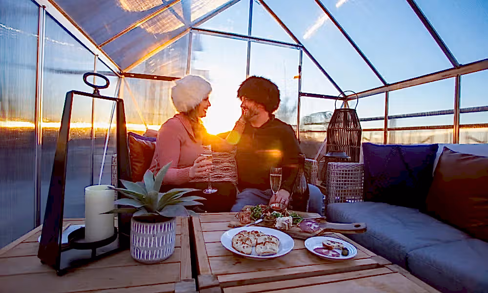 Couple in fuzzy hats drinking champagne in chalets.