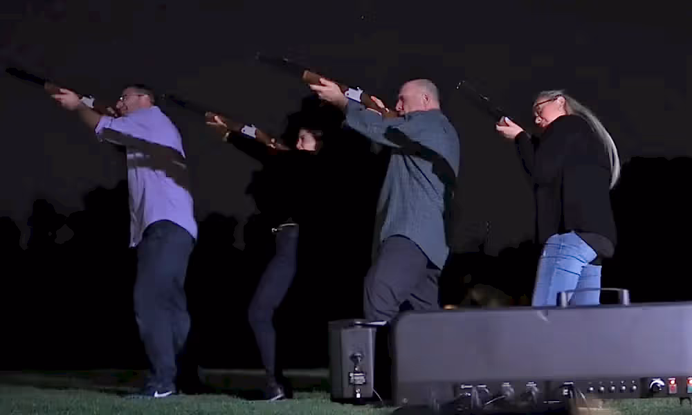 Group of people pointing laser clay guns during night.