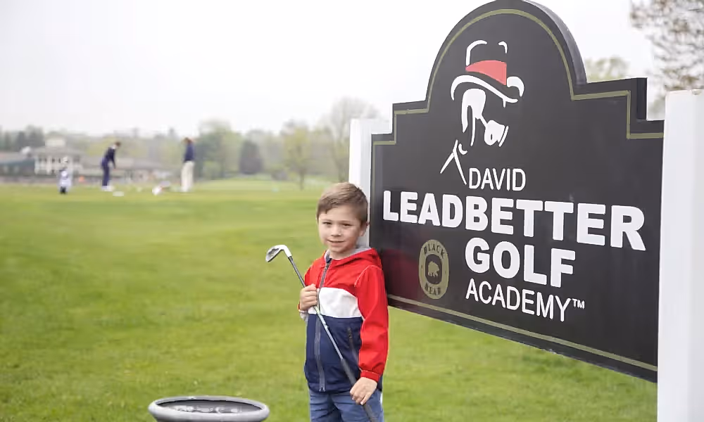 Young boy standing in front of the Leadbetter Golf Academy sign