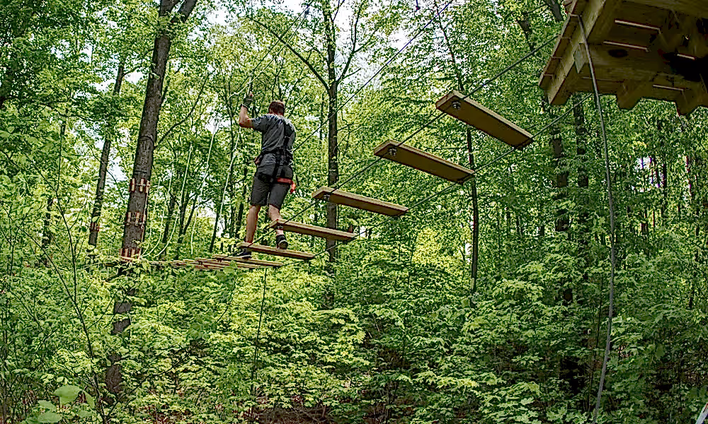Man walking on wooden slats in tree ropes course.