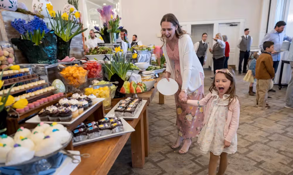 Woman and child holding hands and looking at buffet of food. 