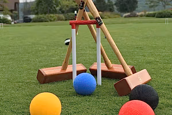 4 croquet balls on the grass and 3 croquet mallets leaning against a wicket