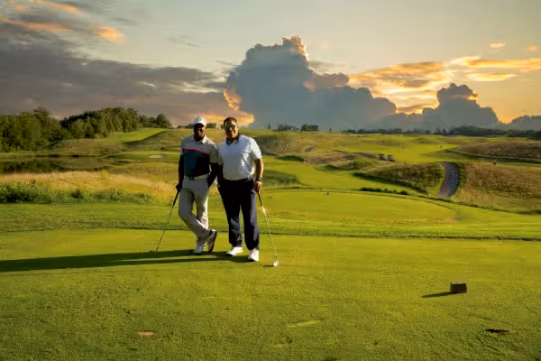 Two golfers stand on Ballyowen Golf Course with sunset behind them.