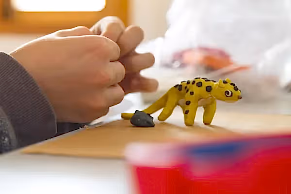 Hands molding yellow clay into animal.