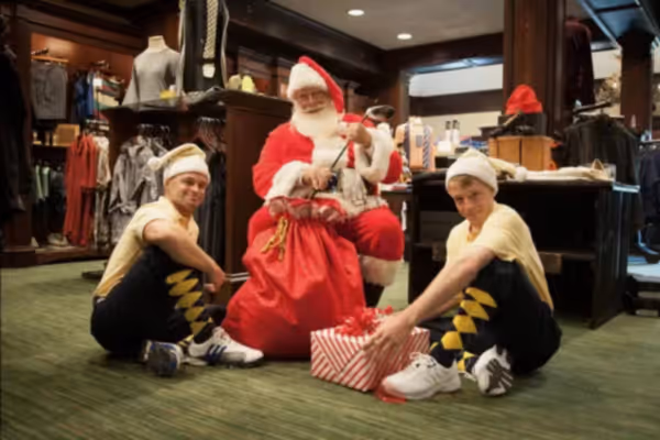 Two men dressed as elves with Santa and his sack of presents in the Crystal Springs Pro Shop