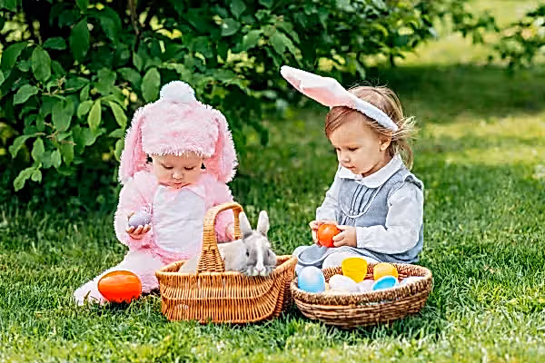 Two very young children dressed up in bunny outfits playing with eggs.
