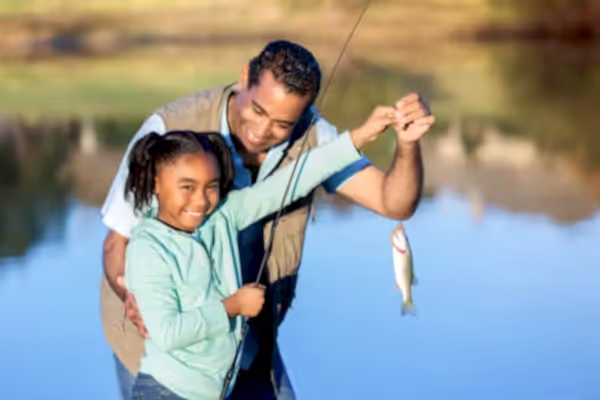 Young girl and older gentleman holding a fish at a pond.
