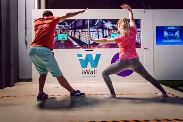 Two people working out in front of iwall machine.