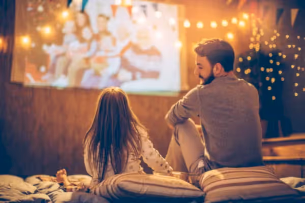 Father and daughter watching movie outdoors on screen under twinkly lights.