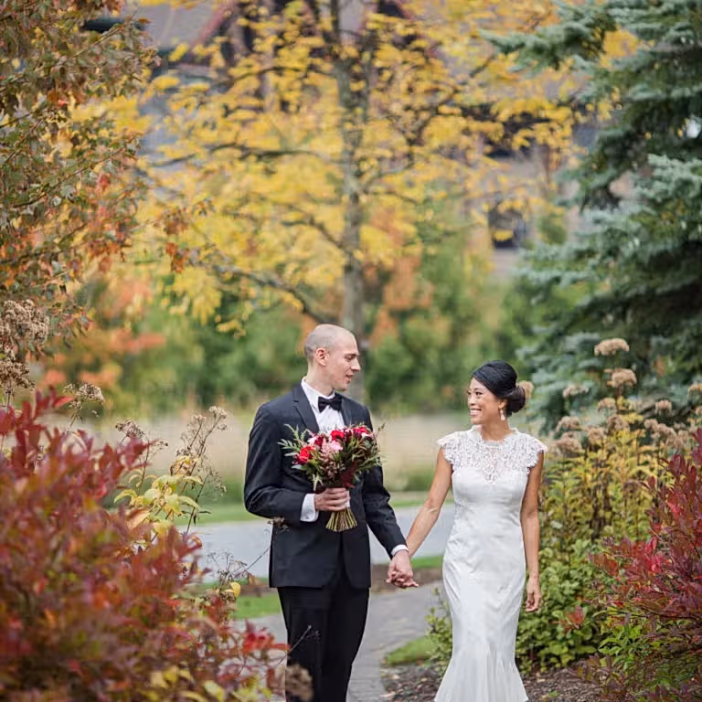 Bride and groom holding hands walking through fall path.