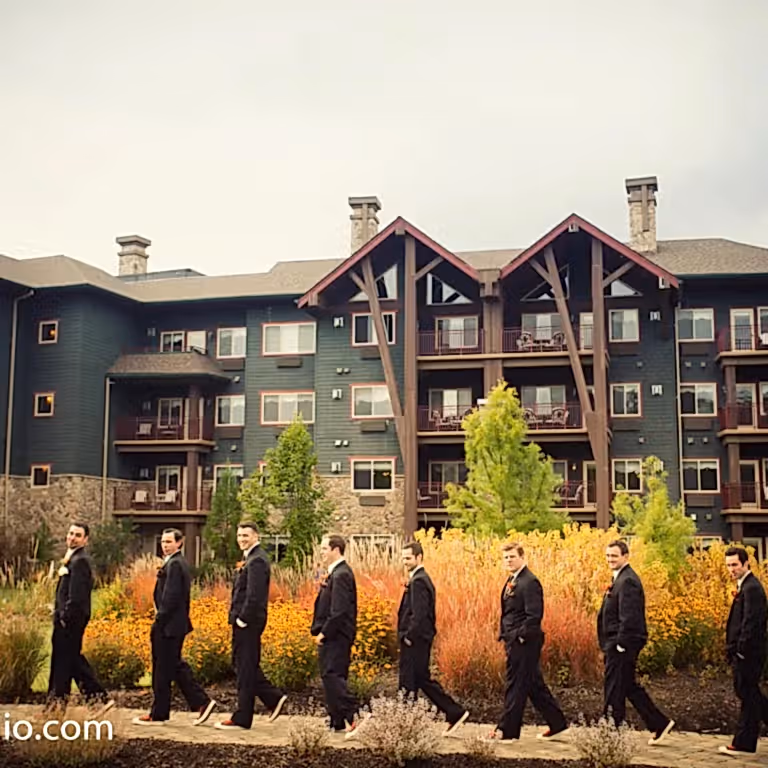 Groom and groomsmen in black tuxes walking in front of Grand Cascades Lodge.