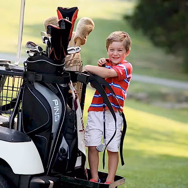 Little boy standing on the back of a golf cart