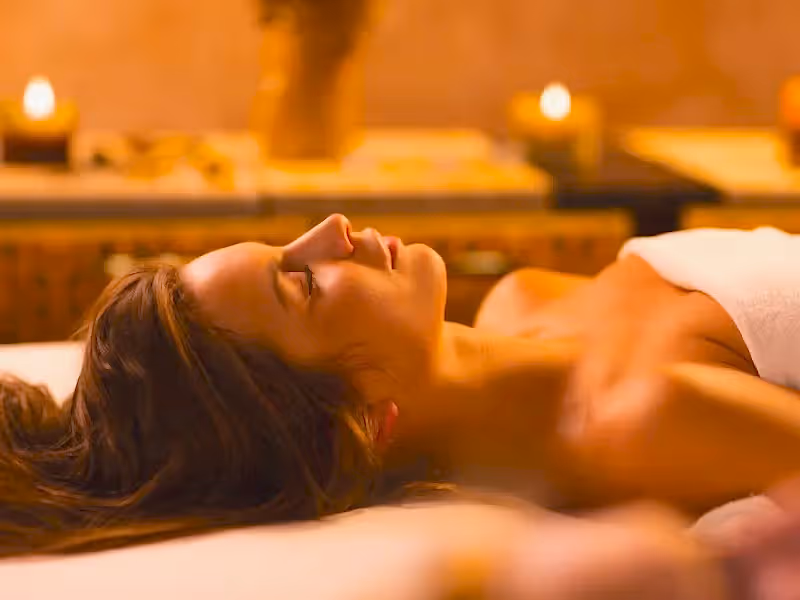 Woman laying in white towel on spa table surrounded by candles.