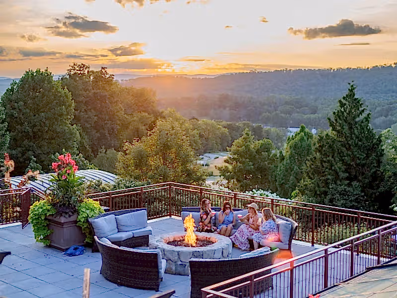 Group of four girlfriends sitting around firepit on Fire & Water terrace overlooking sunset mountain views.