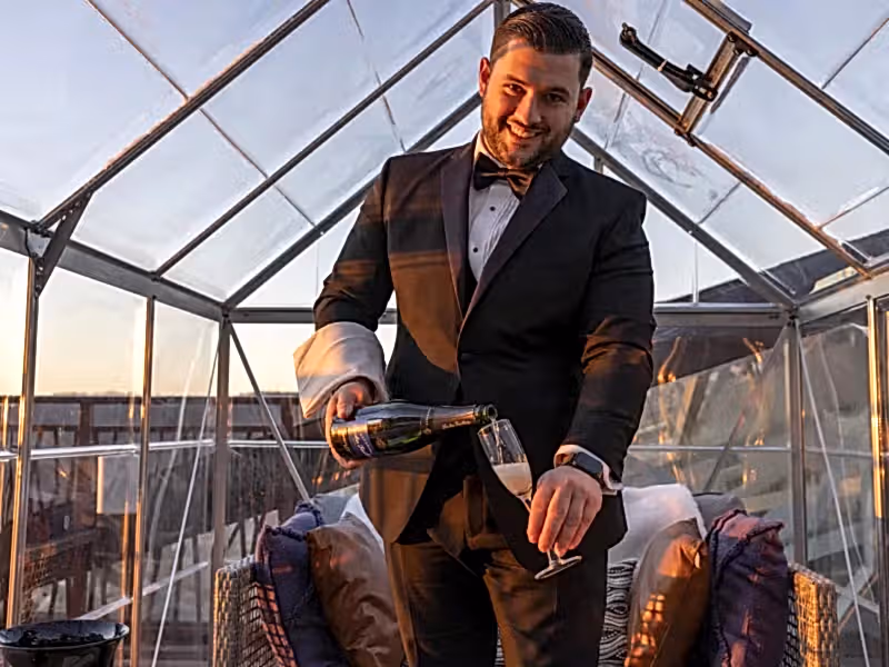 Waiter, dressed in a black suit,  pouring champagne while standing in the champagne chalet. 